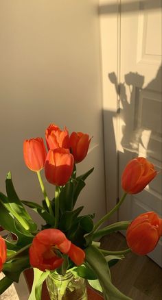 an arrangement of orange tulips in a glass vase on a wooden table next to a door