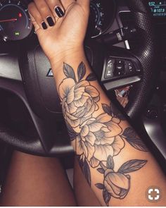 a woman's arm with flowers on it and a steering wheel in the background