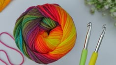 a ball of yarn next to two crochet hooks and some knitting needles on a table