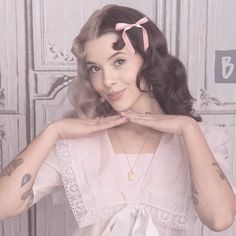 a woman with tattoos and a pink bow in her hair posing for the camera while wearing a white dress