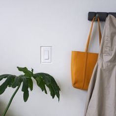 a yellow purse hanging on the wall next to a white coat rack and a green plant