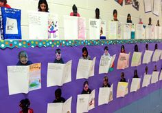 many children are holding up their papers on the wall in front of them, all with faces drawn on them