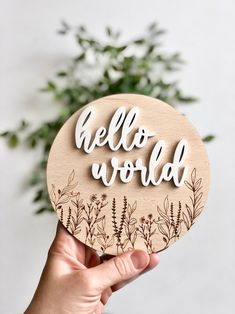 a hand holding up a wooden cutout with the words hello world written on it