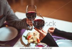 two people toasting glasses of red wine at a dinner table with plates and utensils