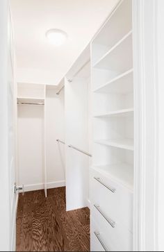 an empty walk in closet with white shelves and drawers on the wall next to it