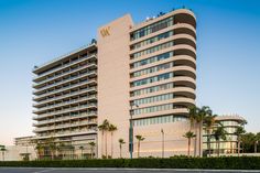 a tall building with palm trees in front of it and a parking lot next to it