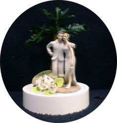 a white cake with a figurine on top of it next to a potted plant