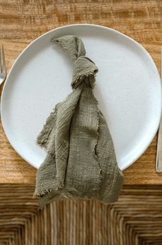 a white plate topped with a piece of cloth on top of a wooden table next to a fork and knife