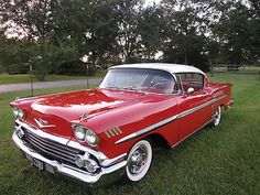 an old red and white car parked in the grass