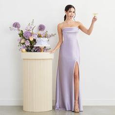 a woman standing next to a table holding a piece of cake in one hand and a cupcake in the other