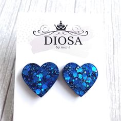 two blue glitter heart shaped earrings on top of a white card with the word diosa written