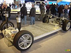 people looking at an electric car on display in a building with many other people standing around it