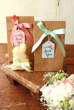 two small gift bags with tags on them are sitting on a wooden table next to flowers