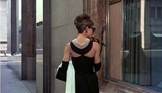 a woman standing on the sidewalk in front of a building wearing a black and white dress