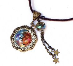 "A necklace with whimsical celestial charm featuring an embossed gold moon and sun pendant that's been accented with violet and pinked orange! Dangling alongside,a couple of star charms swing beneath a lustrous faceted glass bead of light turquoise! And a violet/moonstone-colored Swarovski crystal rhinestone sparkles from the half moons' chin! The artful pendant hangs from a faux suede necklace that has an extender chain to make it easy to find your perfect length! Add this one to your jewelry b Adjustable Brass Sun And Moon Design Jewelry, Adjustable Bohemian Jewelry With Sun And Moon Design, Adjustable Spiritual Charm Necklace With Round Pendant, Adjustable Brass Charm Necklace, Spiritual Pendant Charm Necklace With Adjustable Fit, Spiritual Charm Necklace With Adjustable Round Pendant, Adjustable Round Brass Charm Necklaces, Adjustable Spiritual Pendant Charm Necklace, Vintage Adjustable Moon Necklace