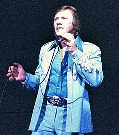 a man in a blue suit is holding a microphone and standing on stage with his hands out