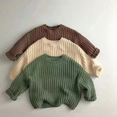 four sweaters are lined up on a white surface, one is green and the other is brown