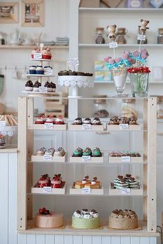 a display case filled with lots of cakes and cupcakes on top of wooden shelves