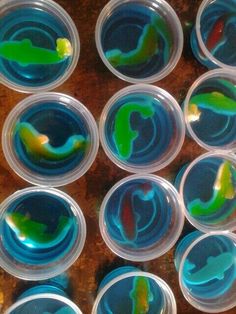 several plastic cups filled with different colored liquids on top of a wooden table next to each other