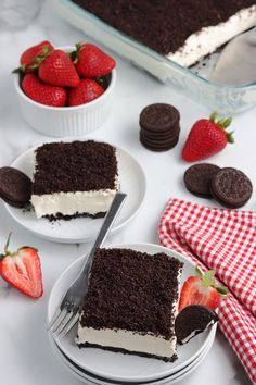 a slice of chocolate cake with white frosting and strawberries on the plate next to it