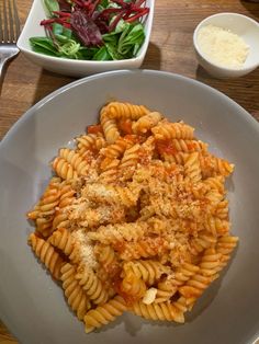 pasta with meat and sauce on a white plate next to a salad in a bowl