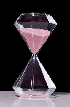 an hourglass sitting on top of a white table next to a black background with pink sand in it