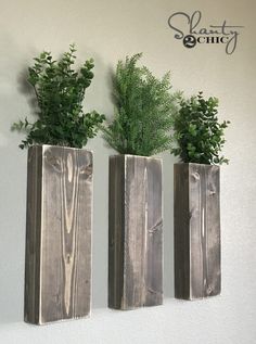 three wooden vases with plants in them hanging on the side of a white wall