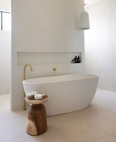 a large white bath tub sitting next to a wooden stool in a bathroom under a light fixture