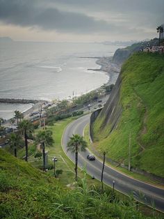 an empty road on the side of a hill next to the ocean with cars driving down it