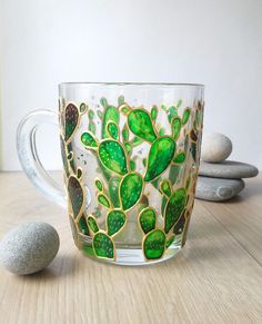 a glass mug with green leaves on it next to some rocks