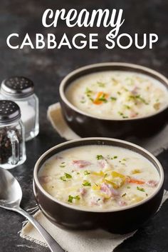 two bowls filled with creamy cabbage soup on top of a black table next to spoons