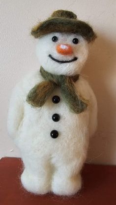 a white snowman with a green hat and scarf on it's head sitting on a table