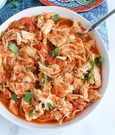 a white bowl filled with shredded meat and tomato sauce on top of a blue table cloth