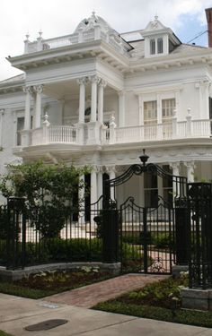 a large white house with many windows and balconies on the second floor, surrounded by black wrought iron fences