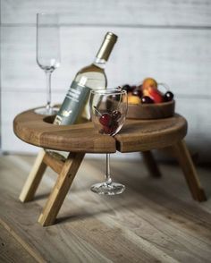 a wooden table with two wine glasses on it and a bowl of fruit in the middle