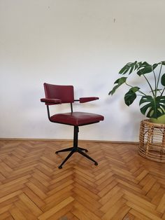 a red chair sitting on top of a wooden floor next to a potted plant