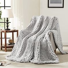 a large chunky knitted blanket sitting on top of a couch next to a lamp