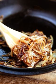 a wooden spatula is being used to stir onions in a skillet