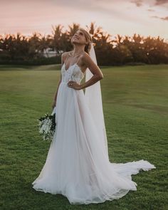 a woman standing in the grass wearing a wedding dress