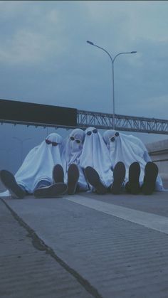 three skateboarders dressed in white cloths sitting on the ground next to a bridge