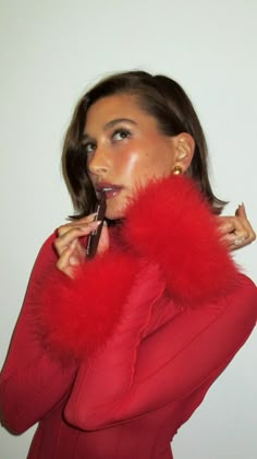 a woman in a red dress is holding a cell phone to her ear and wearing a fur collar