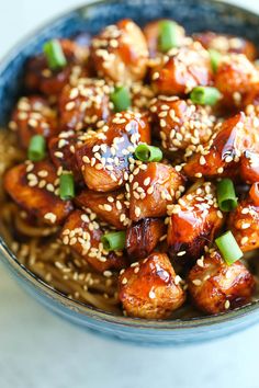 a bowl filled with sesame seed chicken and green onions