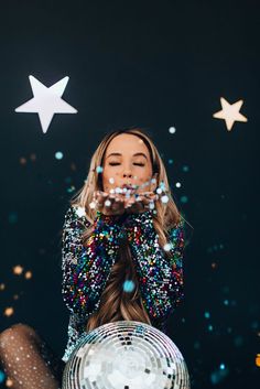 a woman sitting in front of a disco ball with her hands on her face, surrounded by confetti and stars