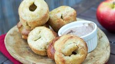 some donuts are sitting on a plate with an apple in the background and dipping sauce