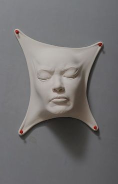 a white mask with eyes closed on a gray surface and red beads around the edges