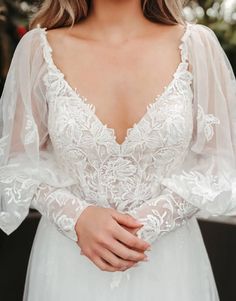 a woman wearing a white wedding dress with sheer sleeves