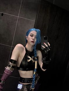 a woman with blue hair holding a cell phone in her right hand and wearing black gloves