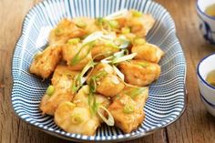 a blue and white plate topped with fried food next to two cups of green tea