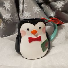 a ceramic penguin mug with a red bow tie on it's head and nose