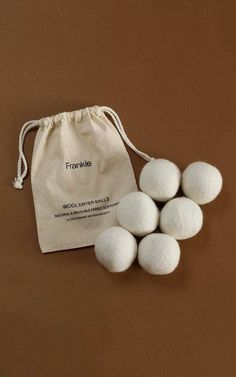 five white wool dryer balls in a drawstring bag on a brown background